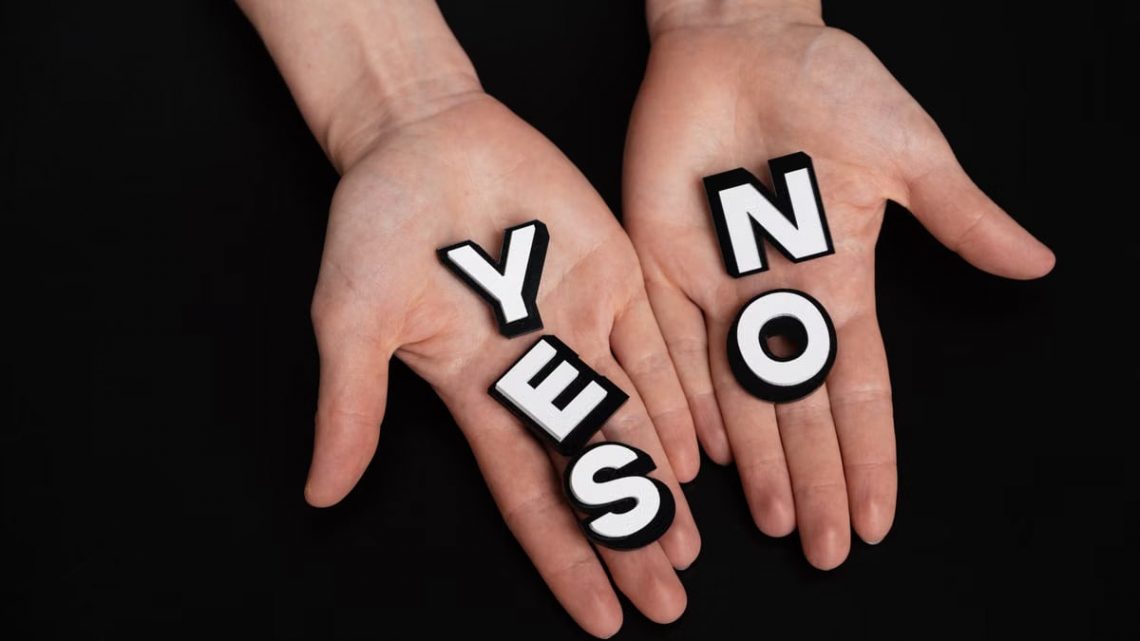 Two hands holding black and white letters spelling 'YES' and 'NO' on a black background.